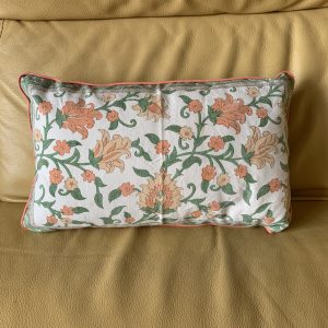 Une taie de coussin rectangulaire avec des motifs floraux corail et verts sur fond écru.